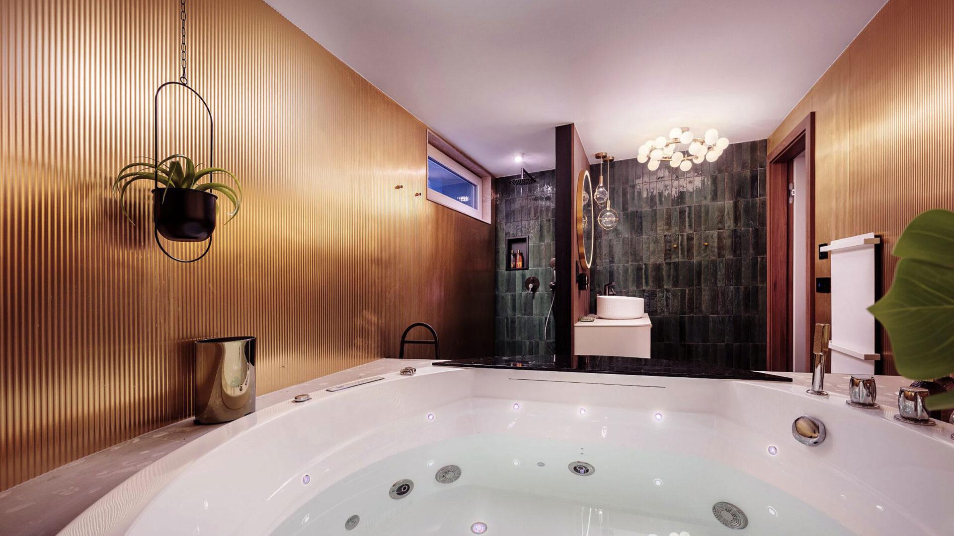 Elements fluted brass laminate wall behind a jacuzzi tub with hanging plants and champagne service