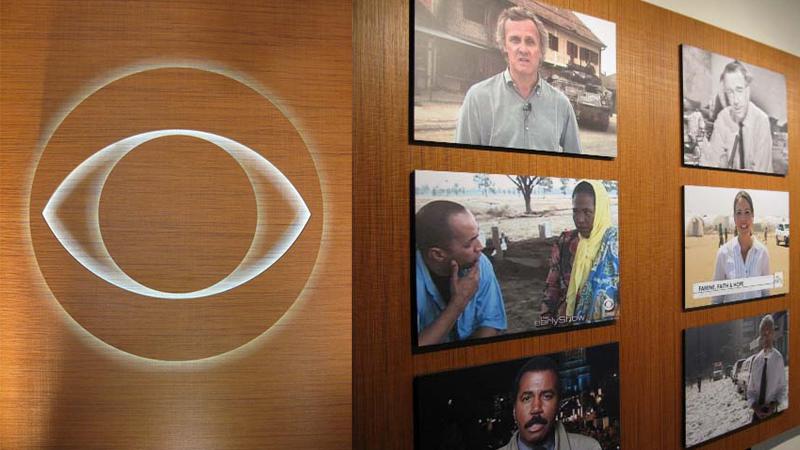 Prensa embossed wood panel cladding an office wall with a backlit CBS eye logo and framed news photography