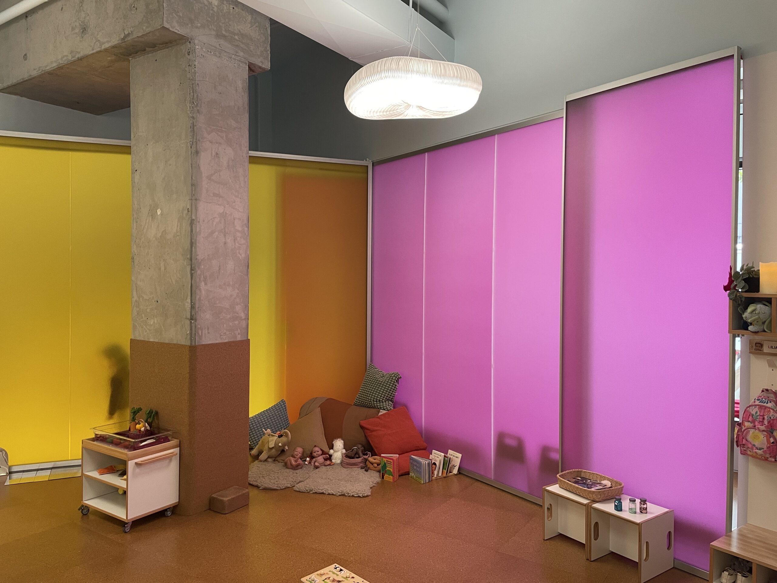 Luminous translucent honeycomb panels in yellow, orange, and magenta forming partition walls around a children's reading nook