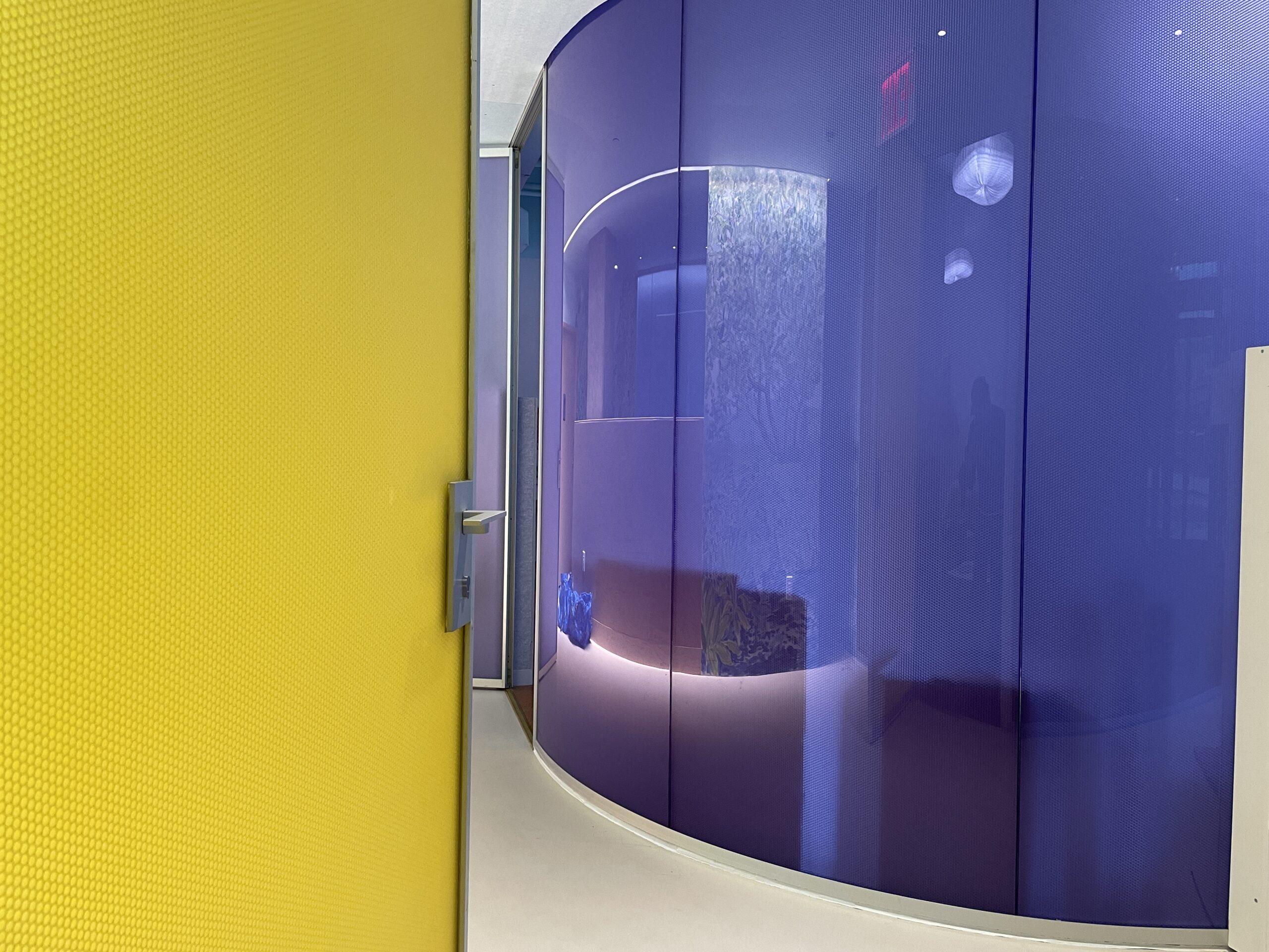Luminous translucent honeycomb panel in yellow forming a curved partition beside a blue-lit entryway