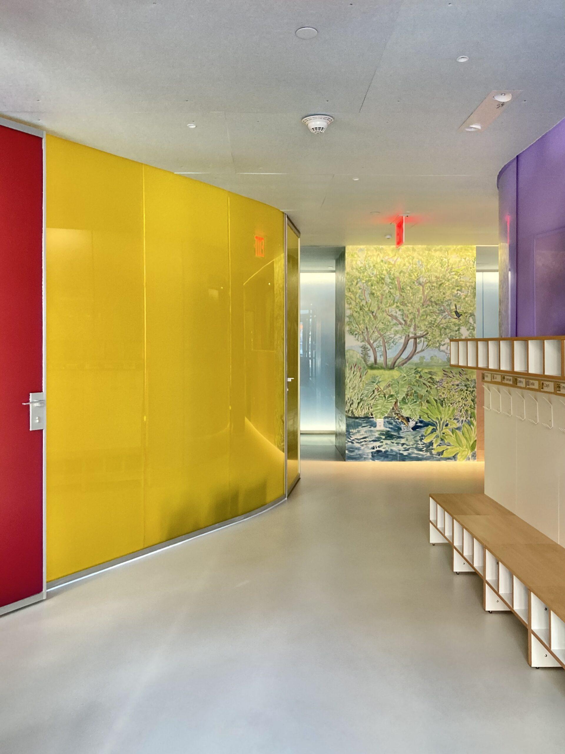 Luminous translucent honeycomb panel in yellow forming a curved hallway wall beside a cubby bench