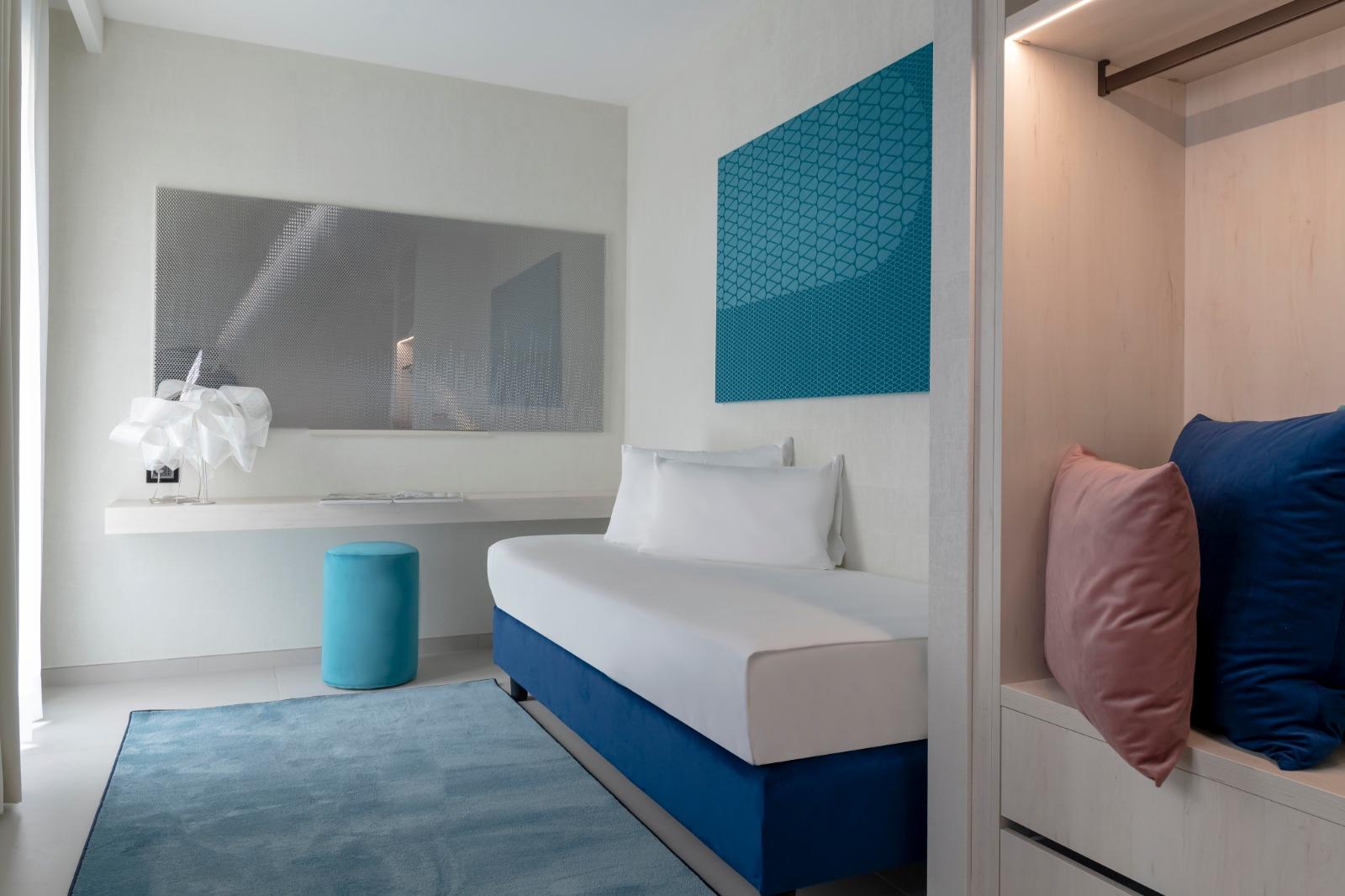 Luminous translucent honeycomb panel in teal mounted above a hotel guest room headboard