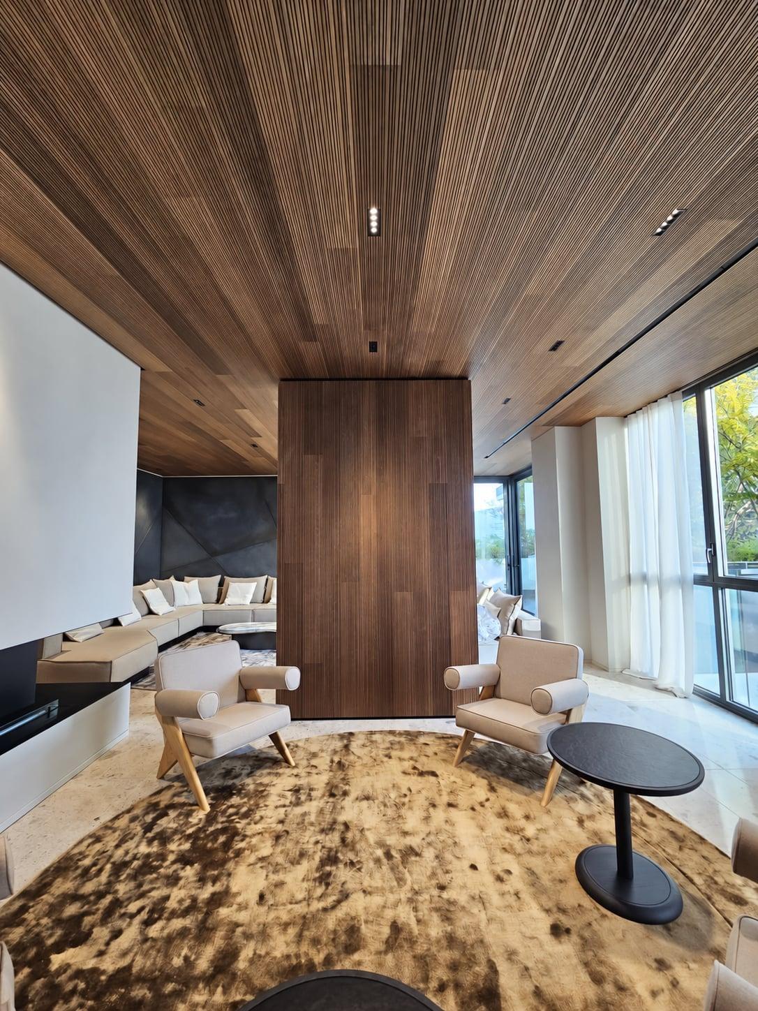 Living room with a ceiling and freestanding column fully clad in walnut-toned Slat fluted wood, above a round rug and lounge chairs
