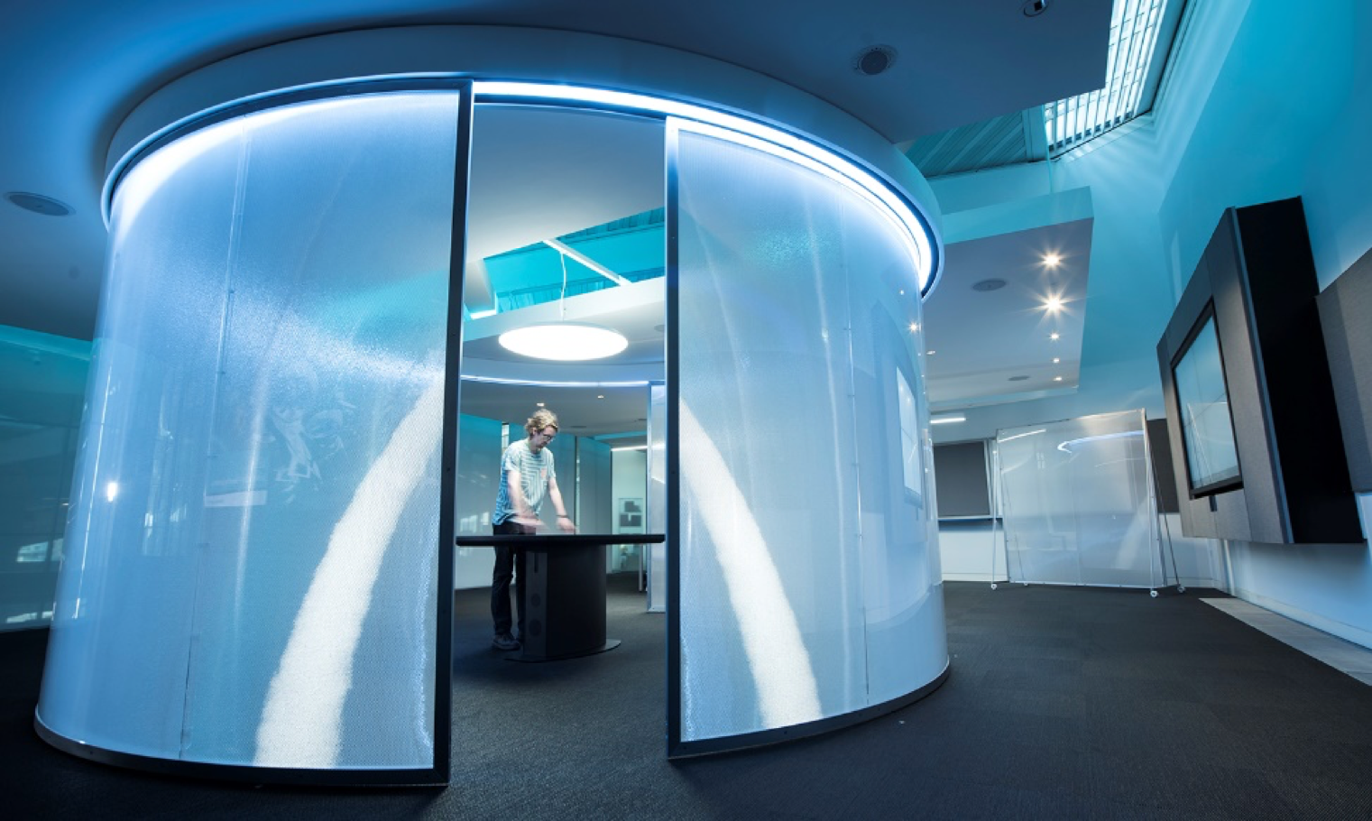 Blue-lit curved Luminous translucent panel forming an enclosed meeting pod in a showroom