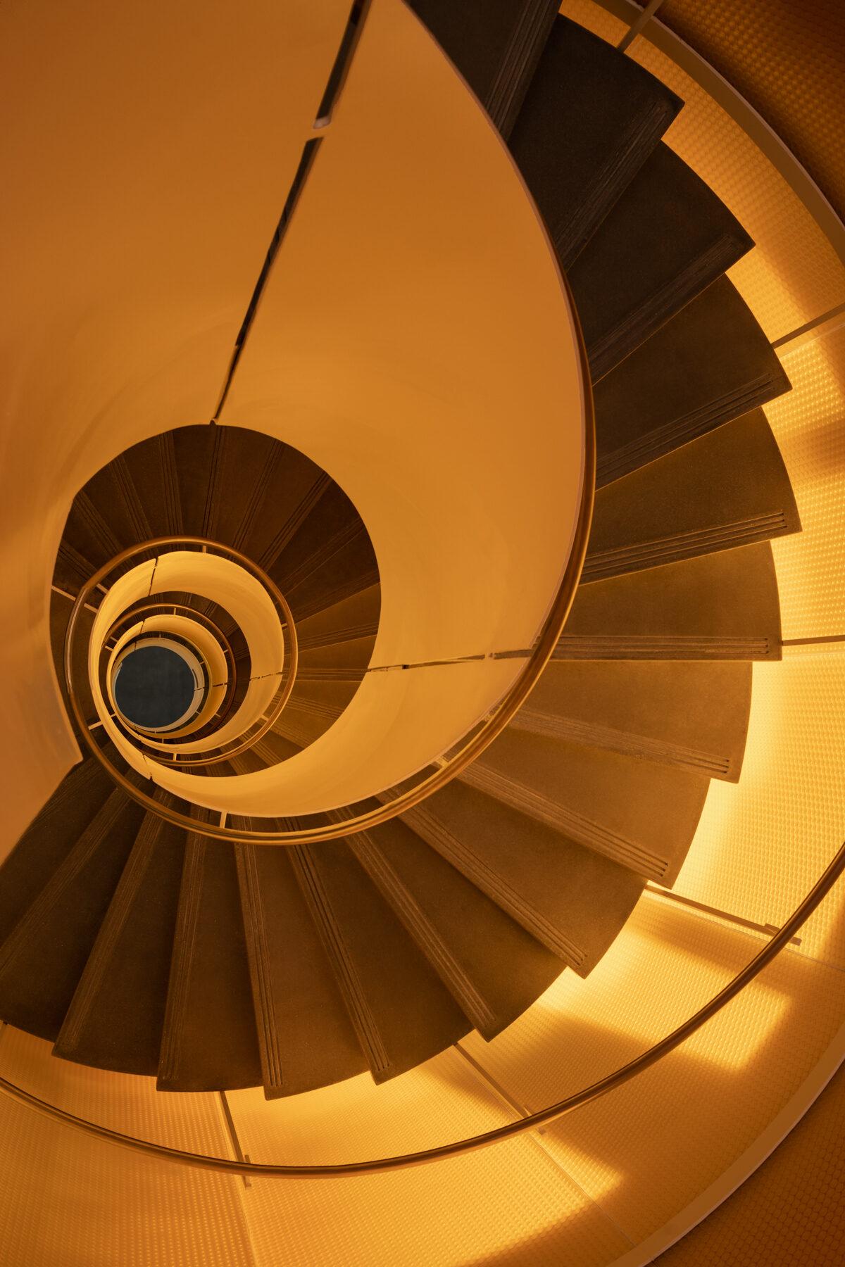 Luminous translucent honeycomb panel backlit in amber, viewed up through a spiral staircase